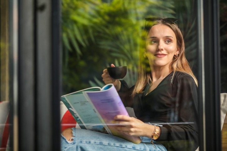 Woman drinking coffee holding a magazine 