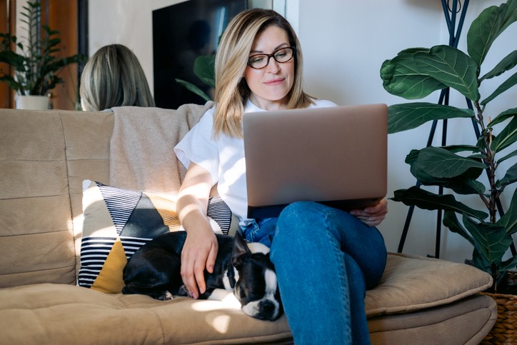 Woman relaxing on couch with dog, with a laptop on her lap